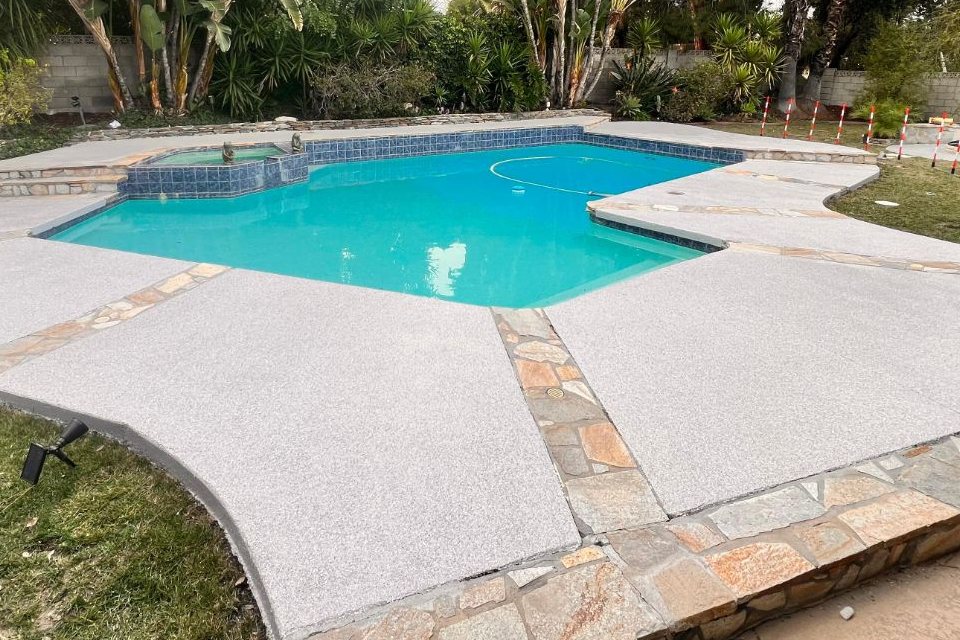 Gray flake pool deck coating with stone borders around a Los Angeles pool